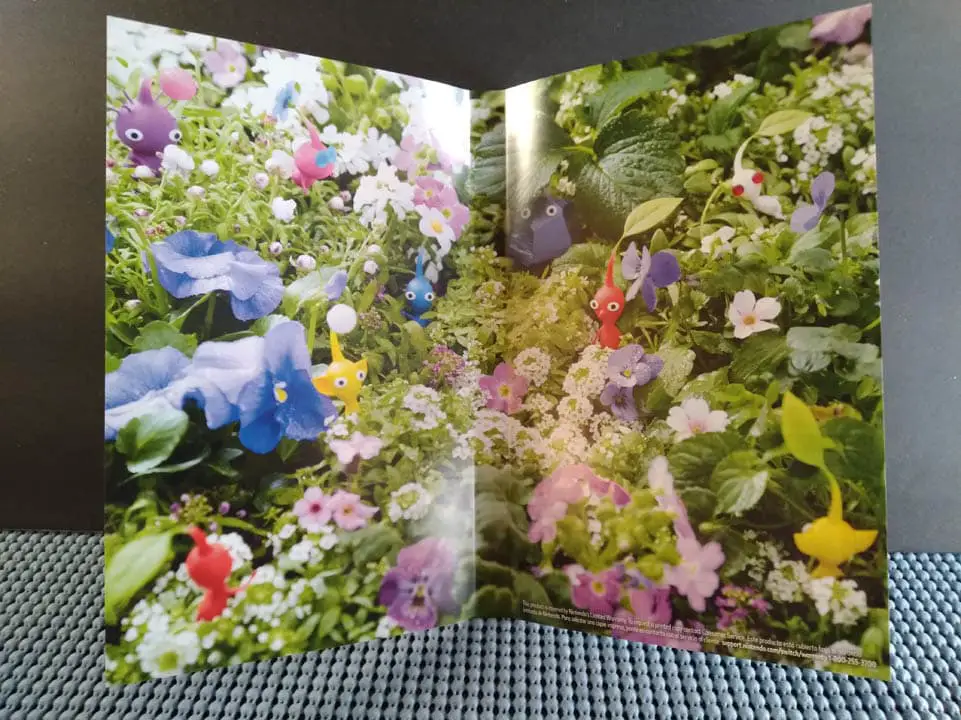 Close-up of Pikmin 3 Deluxe's reversible cover: a green forest setting with Pikmin creatures resting in greenery
