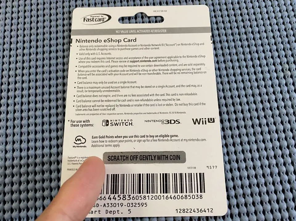 A hand holding a cardboard Nintendo eShop card with a finger pointing at the redemption code