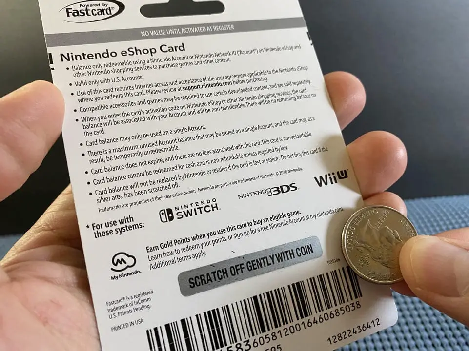 A hand holding a cardboard Nintendo eShop card and a coin