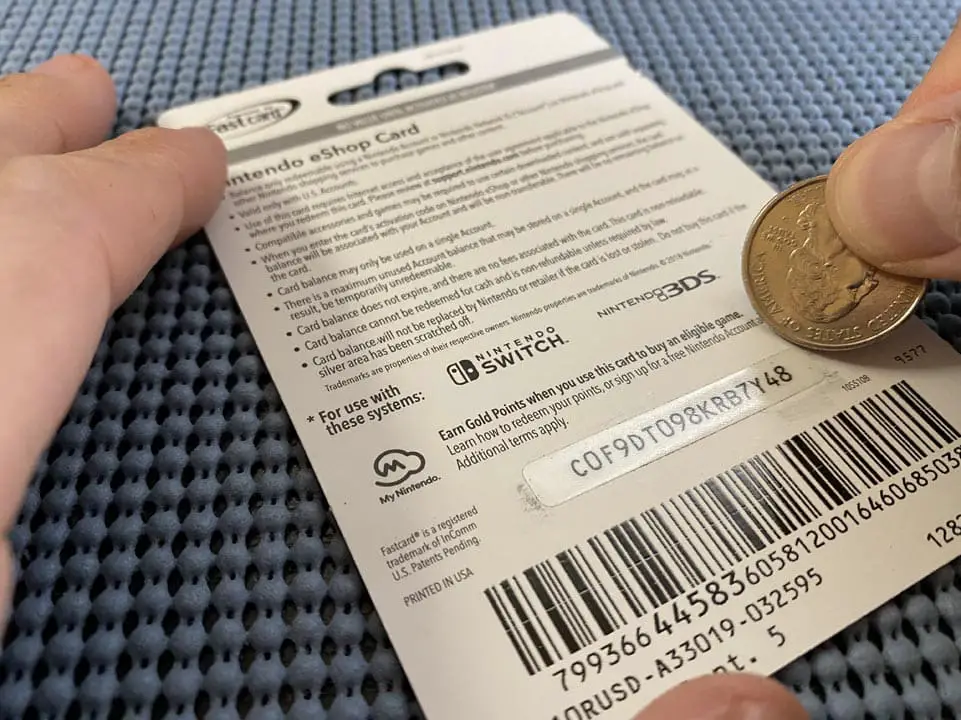 A hand using a coin to scratch the filter over the gift card redemption code