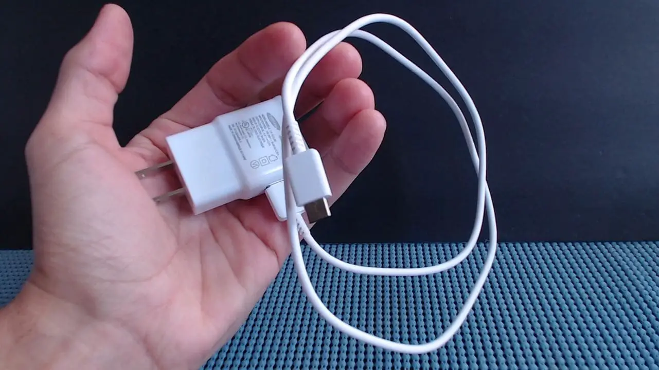A hand holding a white phone charger
