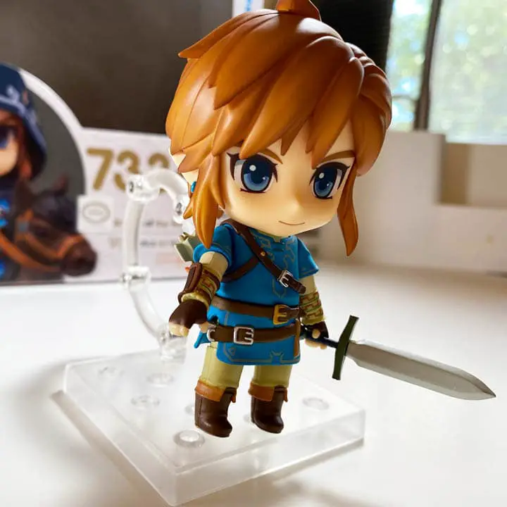 Link figure tstanding upright, holding a sword on a white tabletop (link nendoroid unboxing)