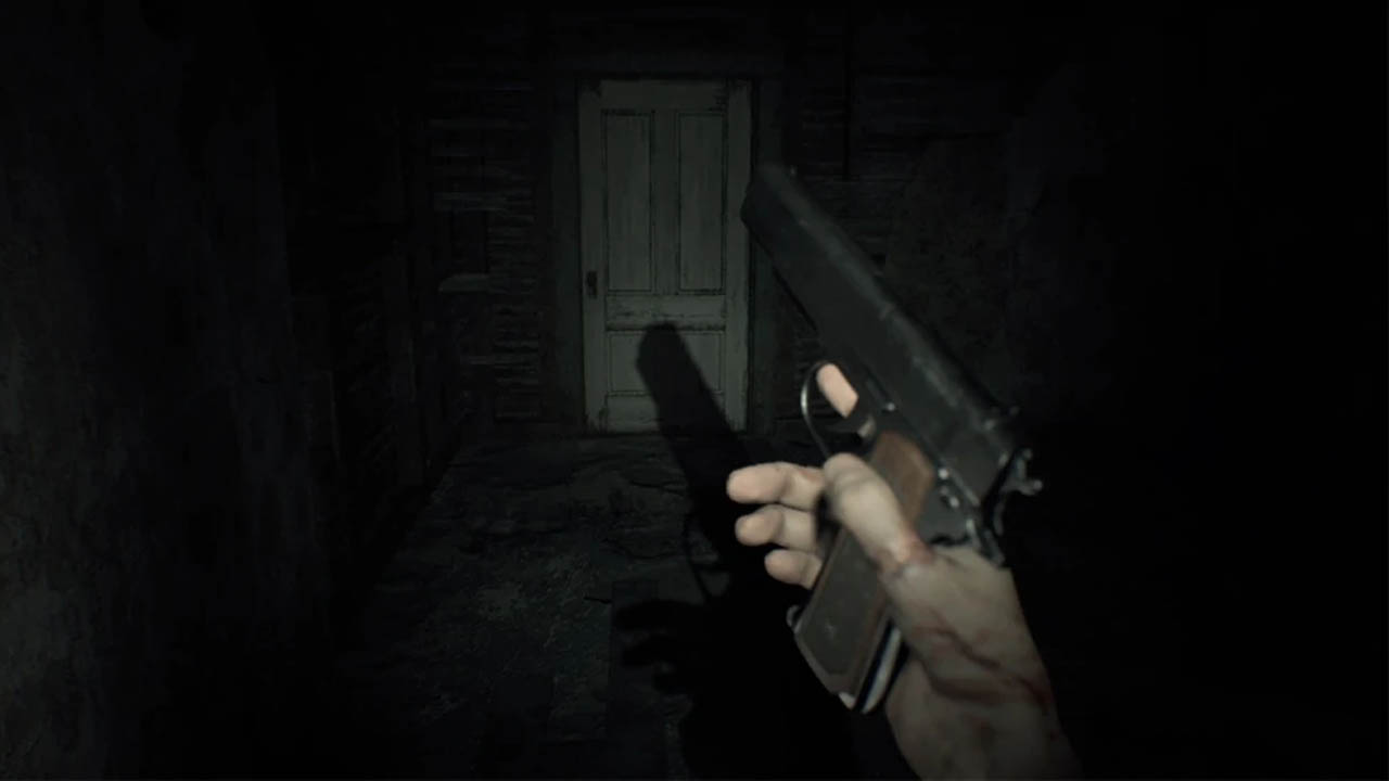 A hand holding a gun in a dimly lit room with a door ahead (resident evil 7 switch version screenshot)
