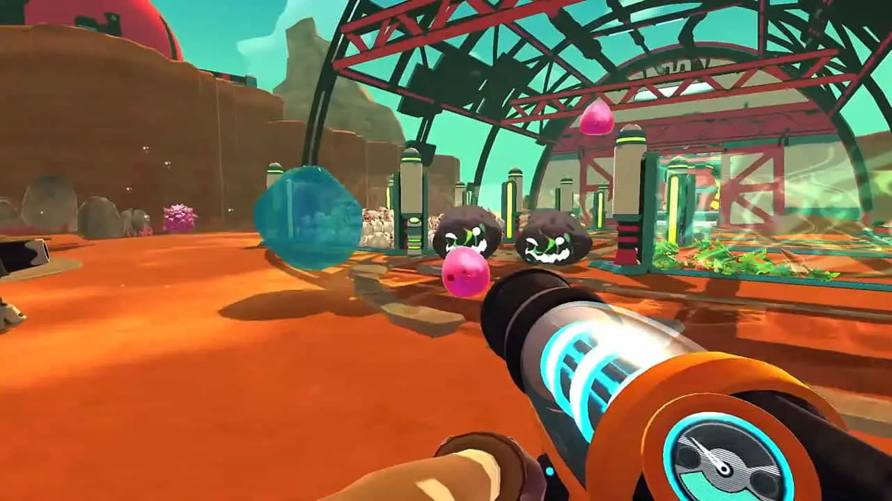 A person holding a gun in a desert with slime monsters in front of him (slime rancher portable screenshot)