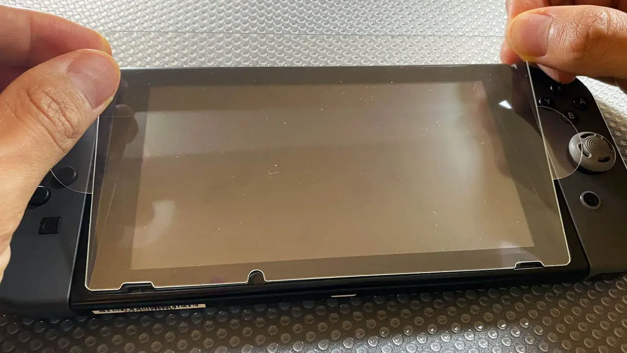 a piar of hands applying a screen protector to a nintendo switch